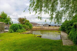 A backyard with a pond, a wooden deck, and a fence.