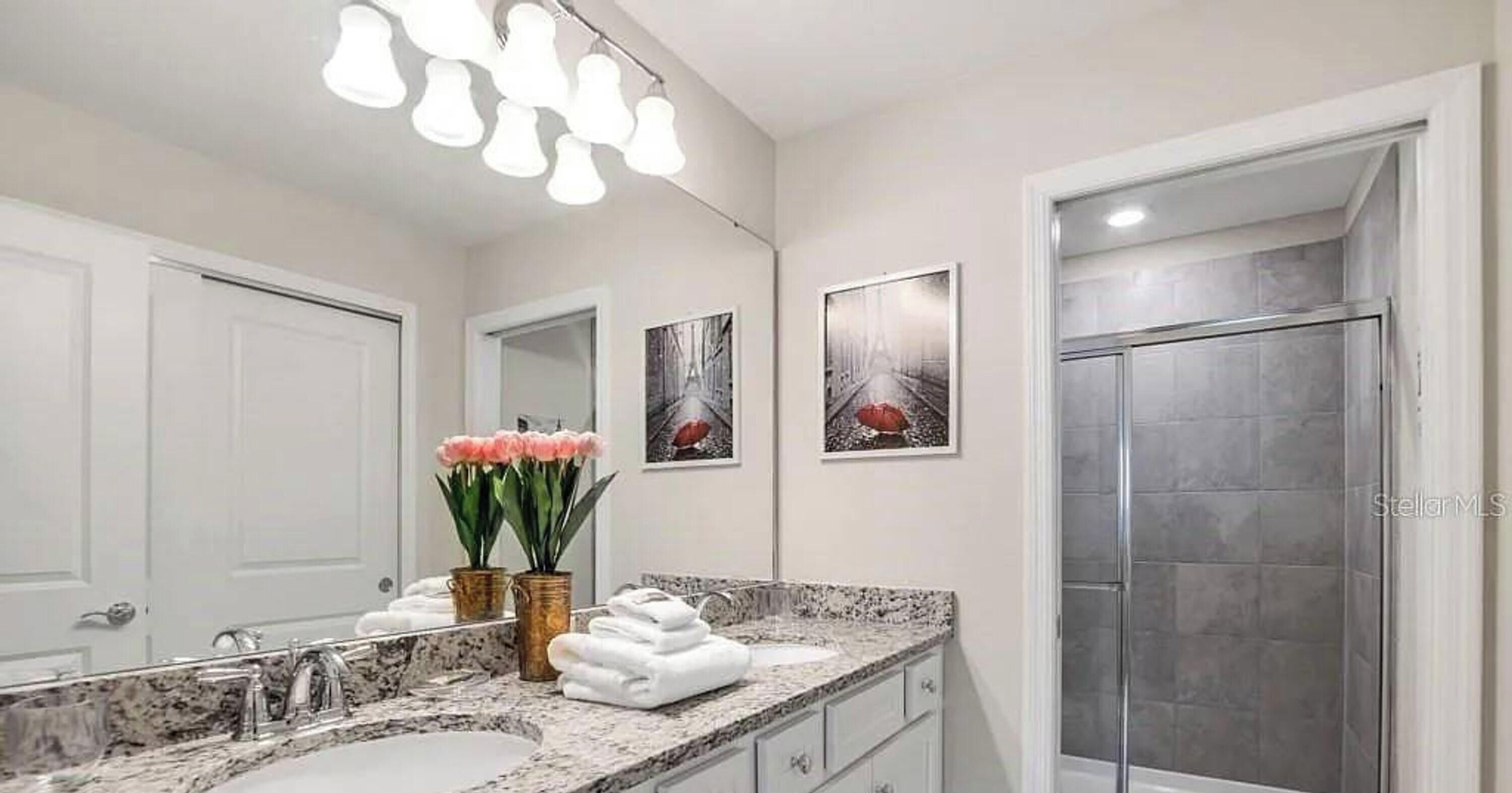 A bathroom with a large mirror, a sink, a shower, and decorative wall art.