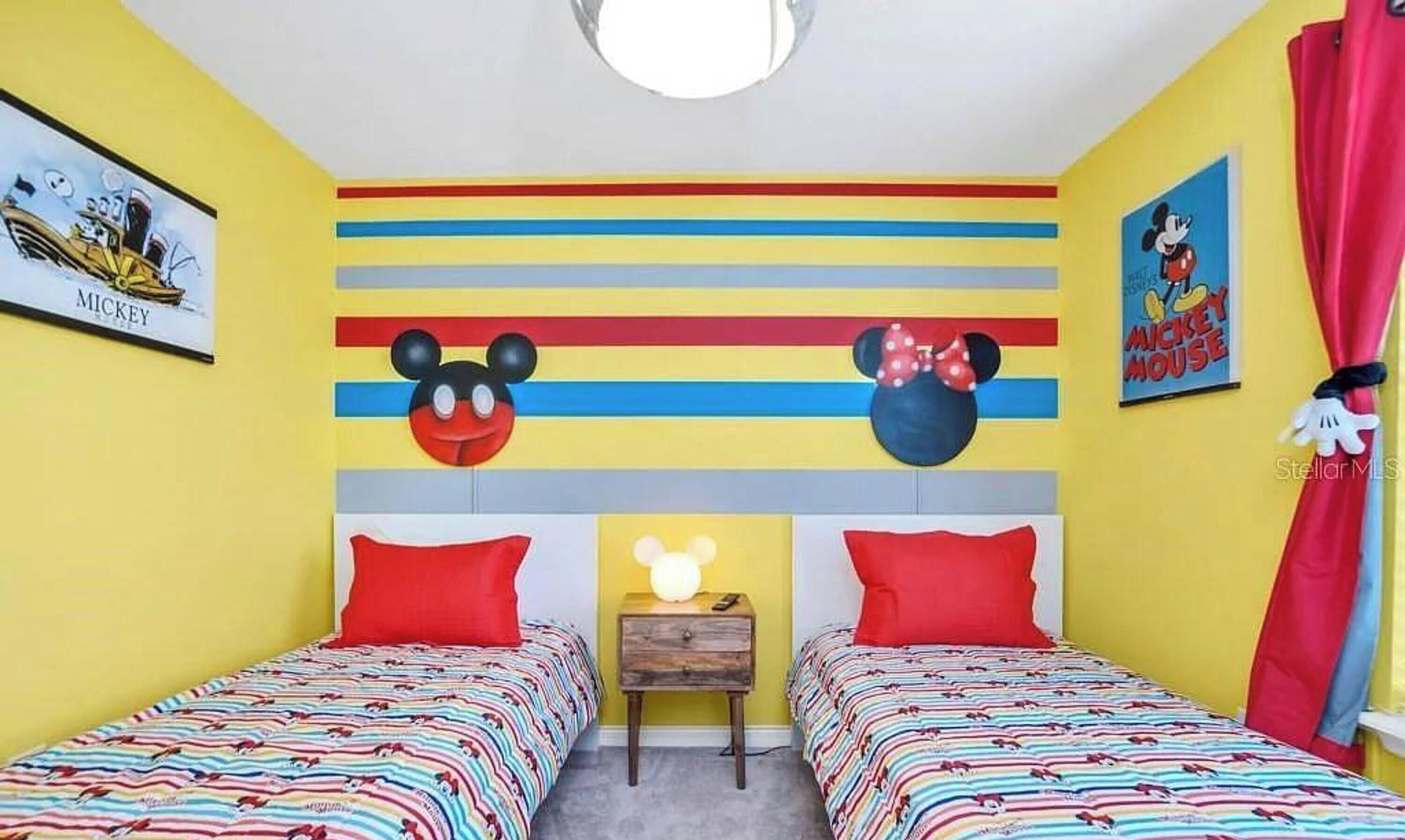 A child's bedroom with two beds, colorful striped bedding, and Mickey Mouse themed decorations.