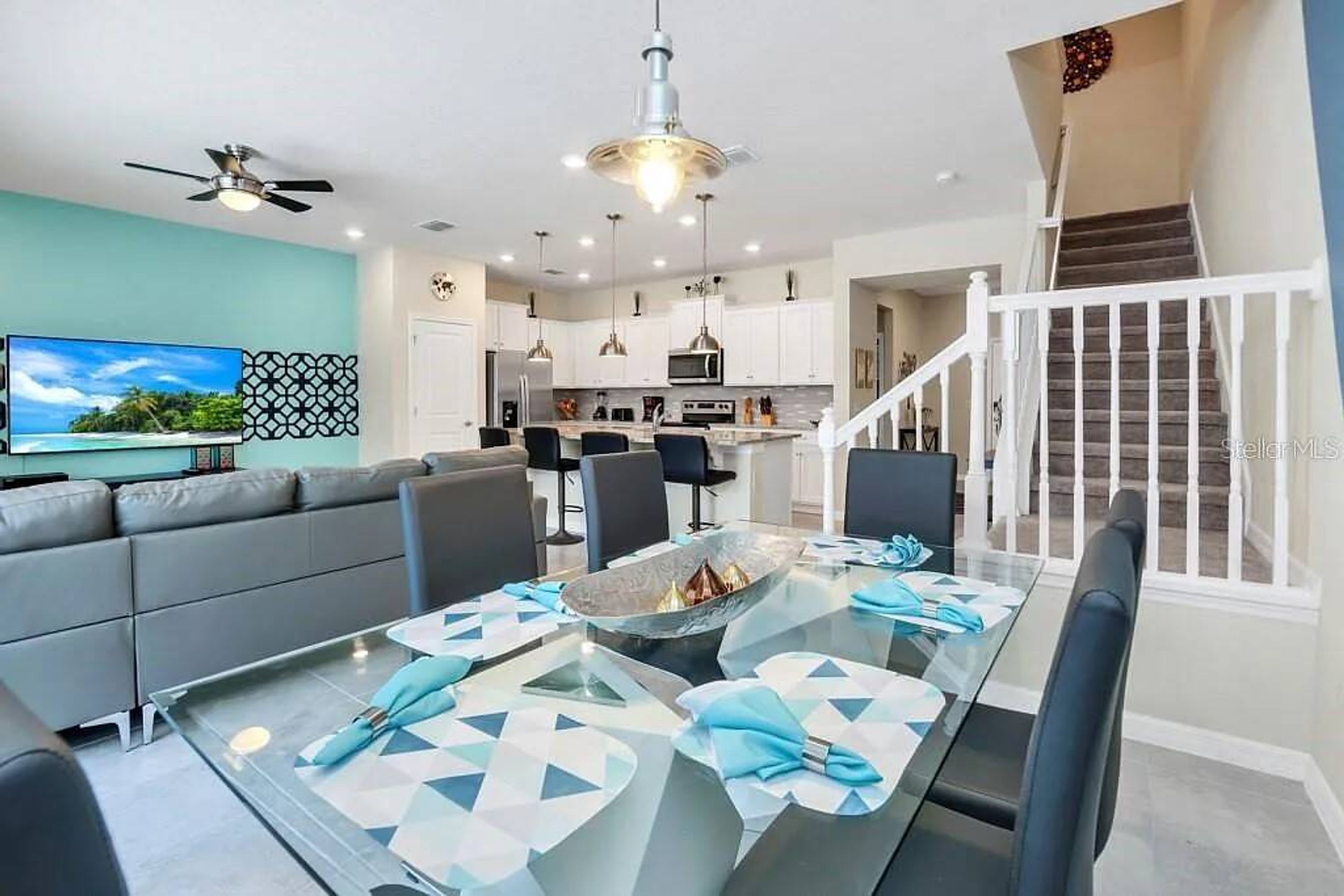 A modern kitchen with white cabinets, a dining area with a glass table, and a staircase.