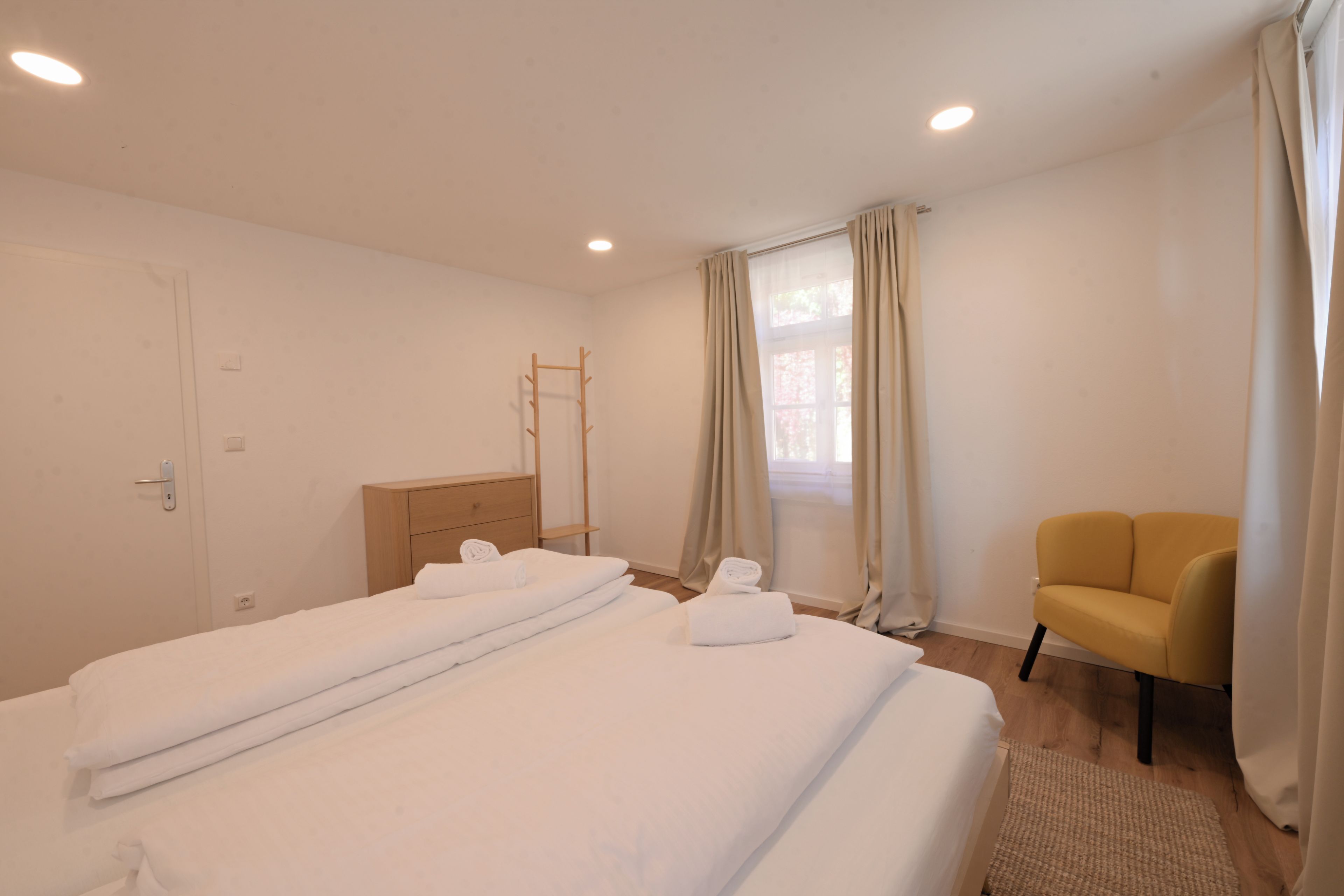 Een hotelkamer met een bed, een stoel, een raam met gordijnen en een houten trap.