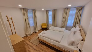 A hotel room with a wooden floor, two beds, a chair, and a coat rack.
