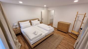 Een hotelkamer met een tweepersoonsbed, een houten dressoir, een kapstok en een nachtkastje met een lamp.