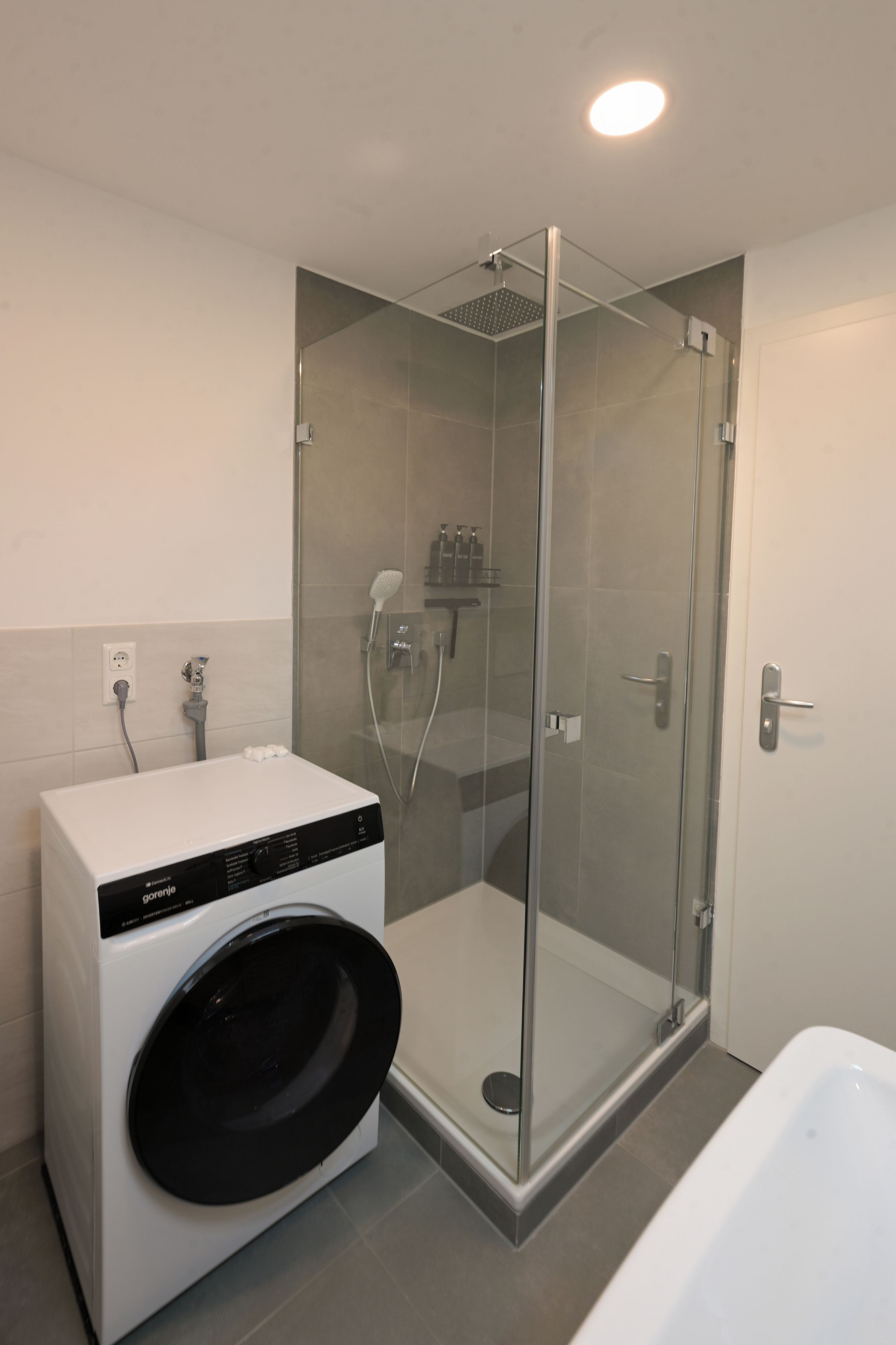 Une salle de bain moderne avec une douche à parois de verre, un lave-linge encastré et une baignoire séparée.