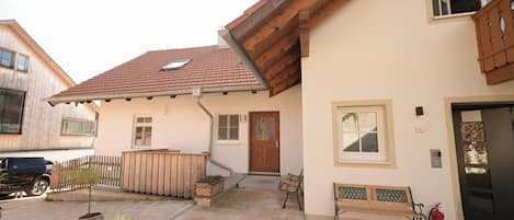 A residential building with a sloped roof, a wooden deck, and a front door.