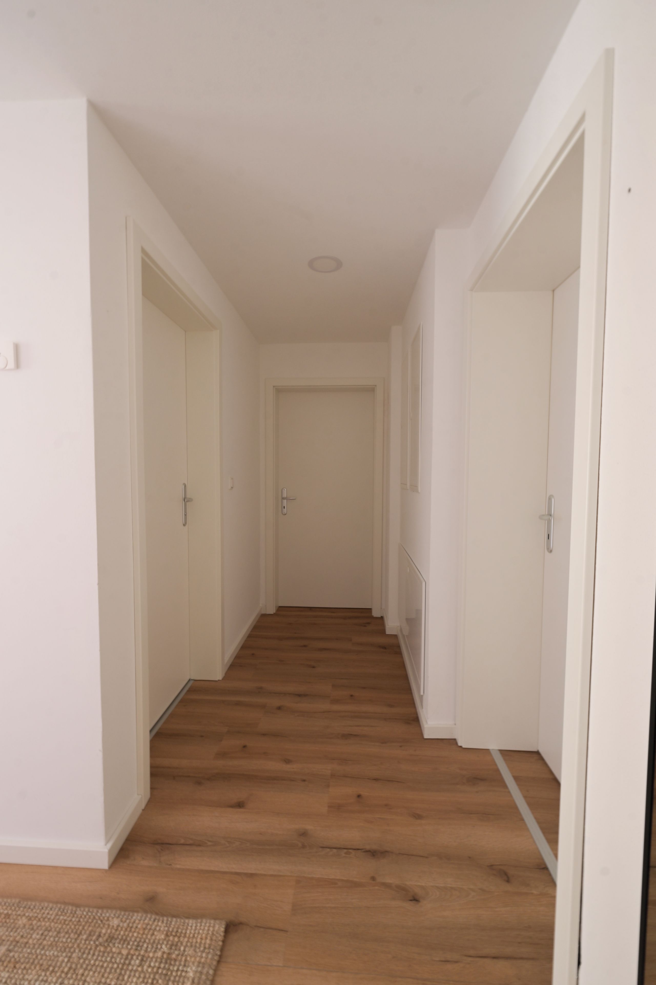 Un couloir doté d’un plancher en bois, de murs blancs et de portes donnant accès aux pièces.