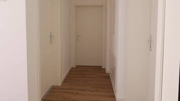 Un couloir doté d’un plancher en bois, de murs blancs et de portes donnant accès aux pièces.