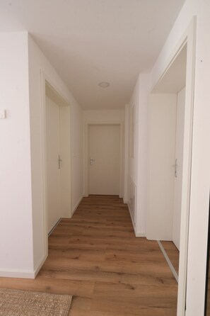 Un pasillo con piso de madera, paredes blancas y puertas que dan a habitaciones.