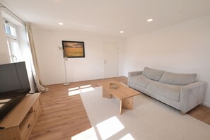 A living room with a sofa, a wooden coffee table, a TV, and a floor lamp.