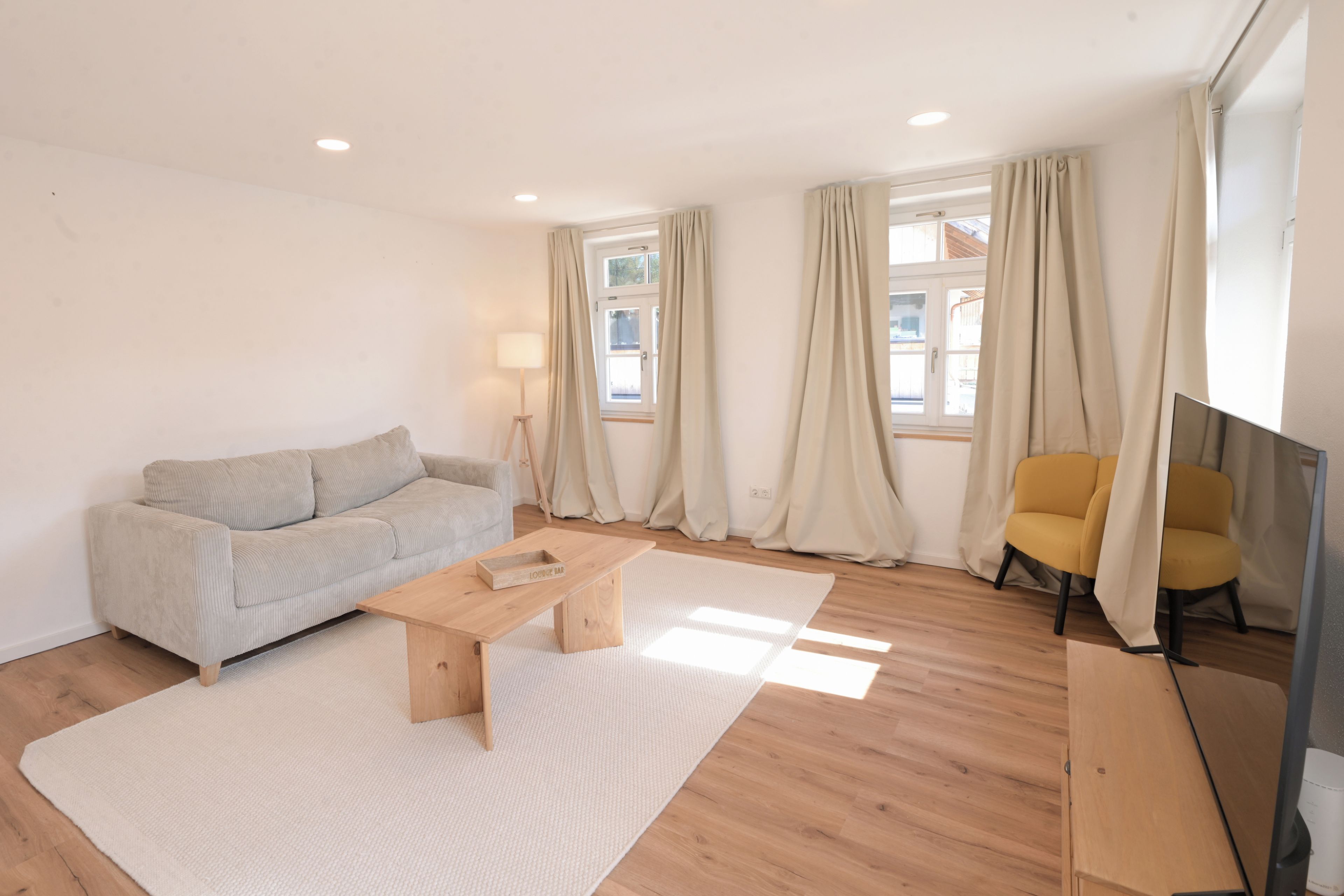 A modern living room with a sofa, a coffee table, a lamp, a chair, and a TV.