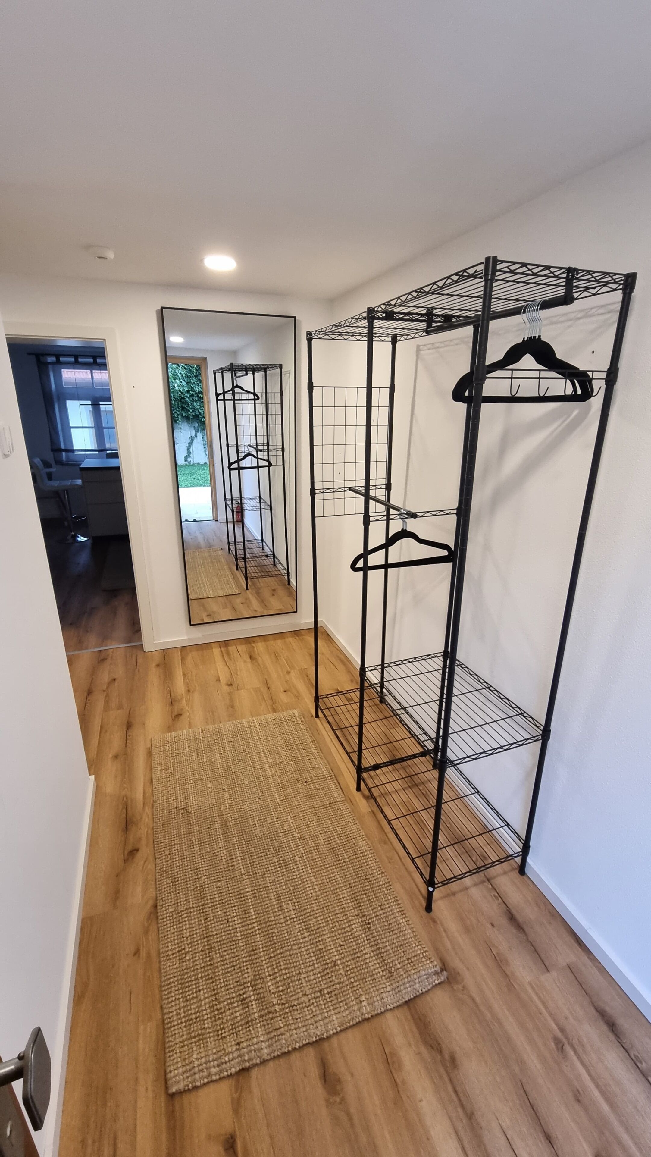 Een gang met een houten vloer, een spiegel en een metalen kledingrek.