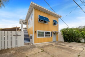 A two-story building with a white picket fence, a small porch, and a garage. - Birdwatch Bungalow Upstairs (Cedar Key)