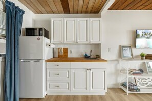 A compact kitchen with white cabinets, a wooden countertop, a built-in microwave, and a sink. - Birdwatch Bungalow Upstairs (Cedar Key)