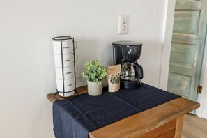 A coffee maker, a stack of coffee cups, a potted plant, and a coffee bag on a table. - Birdwatch Bungalow Upstairs (Cedar Key)