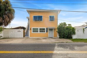 A two-story building with a white picket fence, a front door, and a staircase leading to the second floor. - Birdwatch Bungalow Upstairs (Cedar Key)