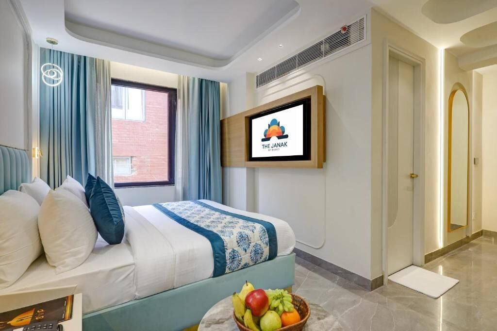 A hotel room with a bed, a television mounted on the wall, and a fruit basket on the floor.