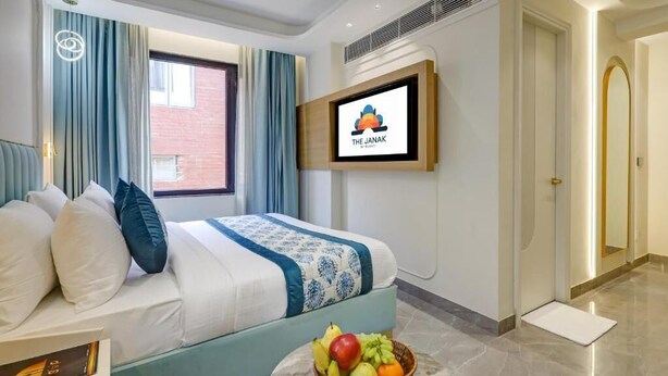 A hotel room with a bed, a television mounted on the wall, and a fruit basket on the floor. - Hotel The Janak by Shanti (New Delhi)