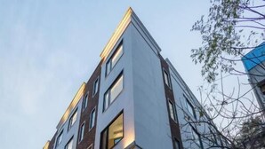 A multi-story hotel with a modern facade, large windows, and a ground-level entrance. - Hotel The Janak by Shanti (New Delhi)