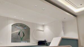 A modern reception area with a curved reception desk, a stone accent wall, and recessed ceiling lighting. - Hotel The Janak by Shanti (New Delhi)