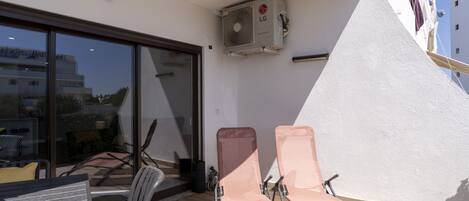 A balcony with two chairs, a table, and an air conditioning unit.