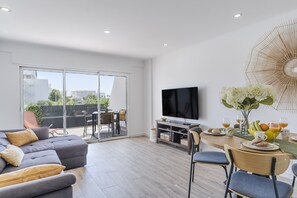 A modern living room with a sofa, television, dining area, and a view of the outdoors. - #410 Sunny Lemon Apartment | Albufeira (Albufeira)