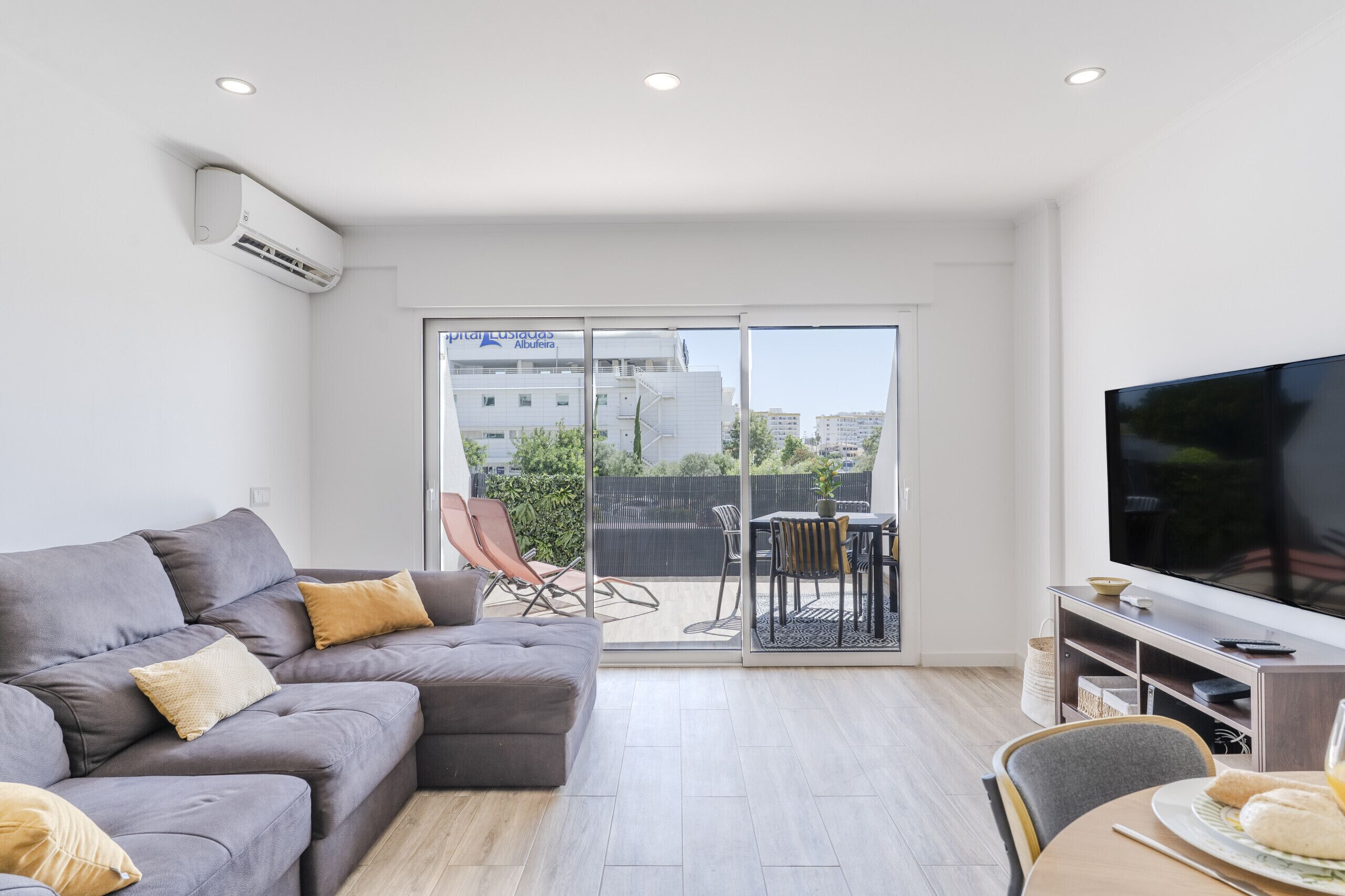 A modern living room with a grey sectional sofa, a flat-screen TV, and a dining area with a table and chairs.