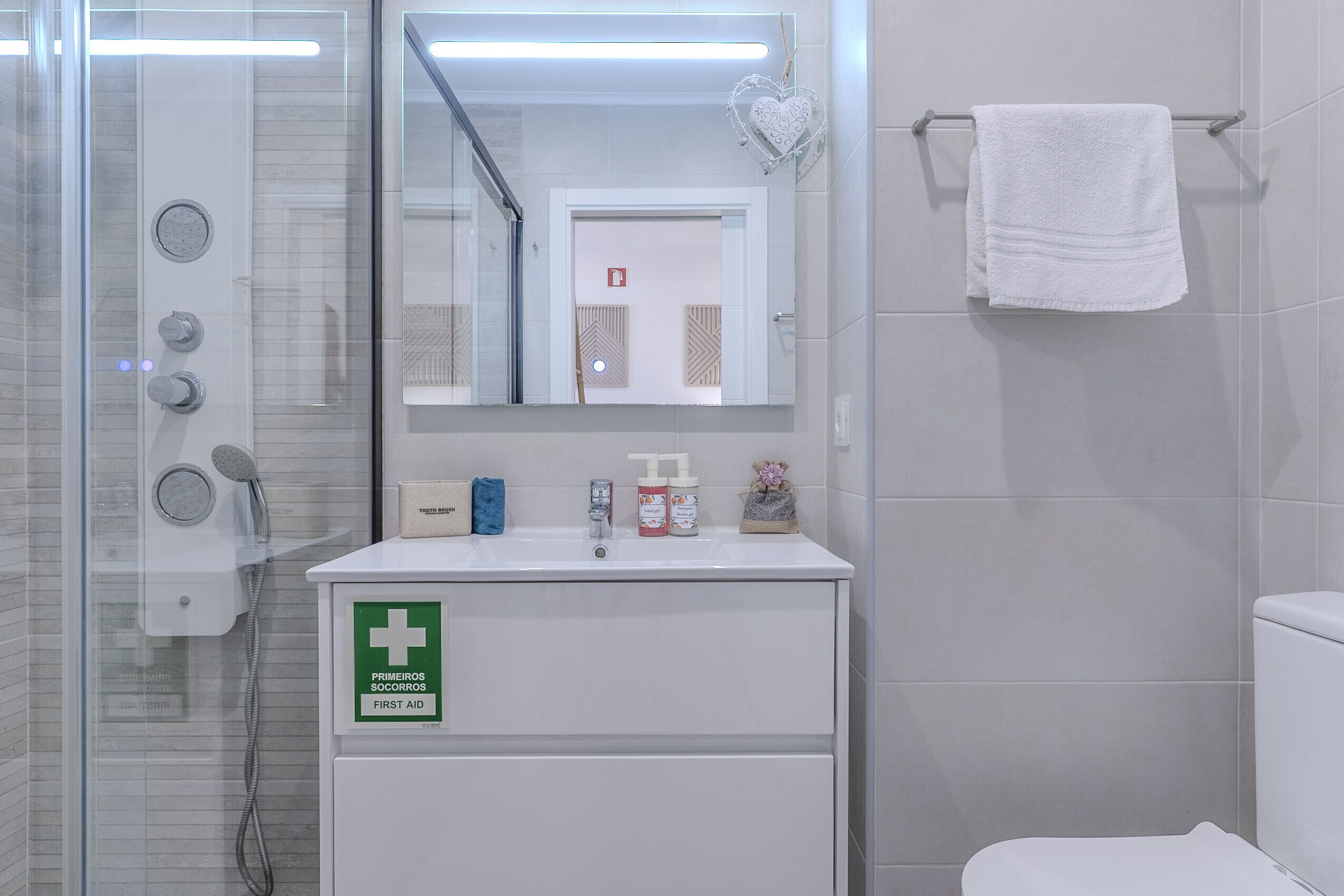 Une salle de bain avec une douche à parois de verre, un lavabo blanc orné d’un symbole de premiers secours et un porte-serviettes avec une serviette blanche.