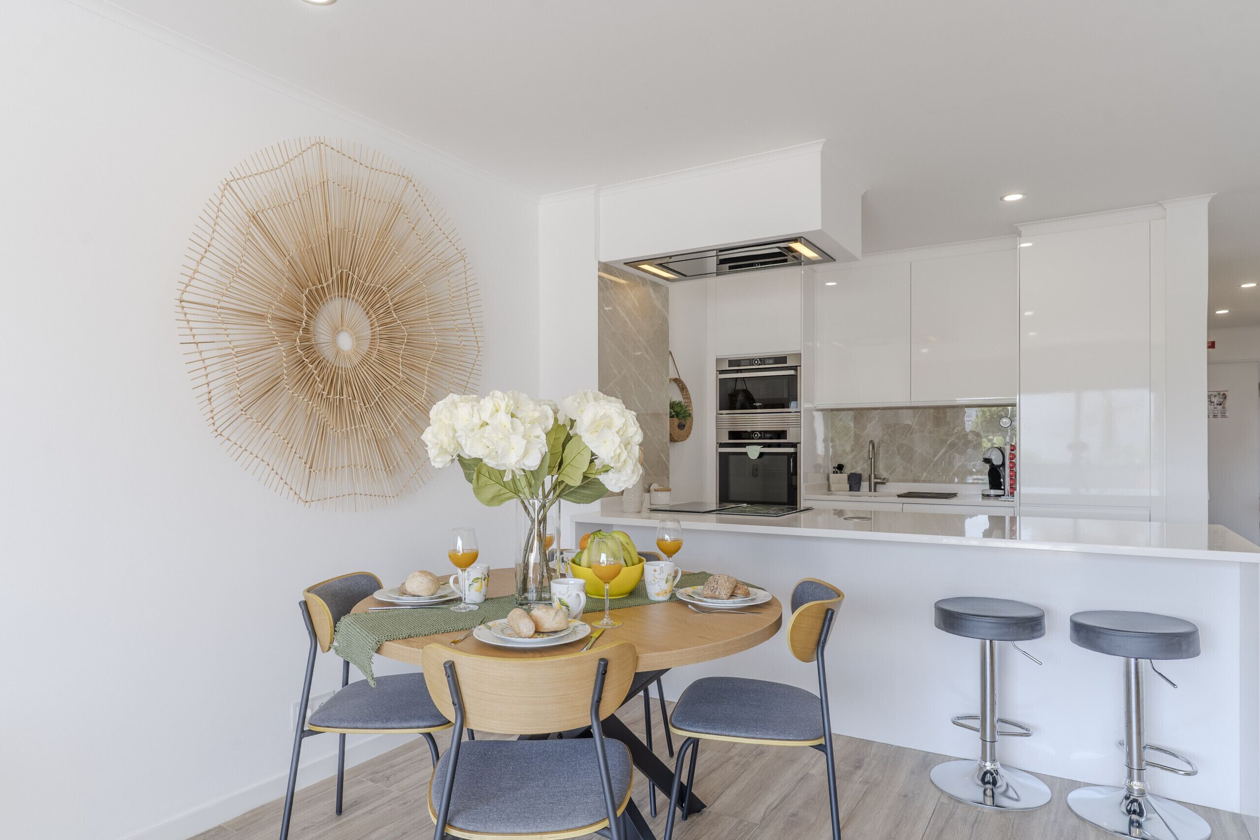 A modern kitchen with white cabinetry, a central island, and a dining area with a round table and four chairs.