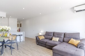 A modern living room with a grey sofa, a dining area with a table and chairs, and a kitchen in the background. - #410 Sunny Lemon Apartment | Albufeira (Albufeira)