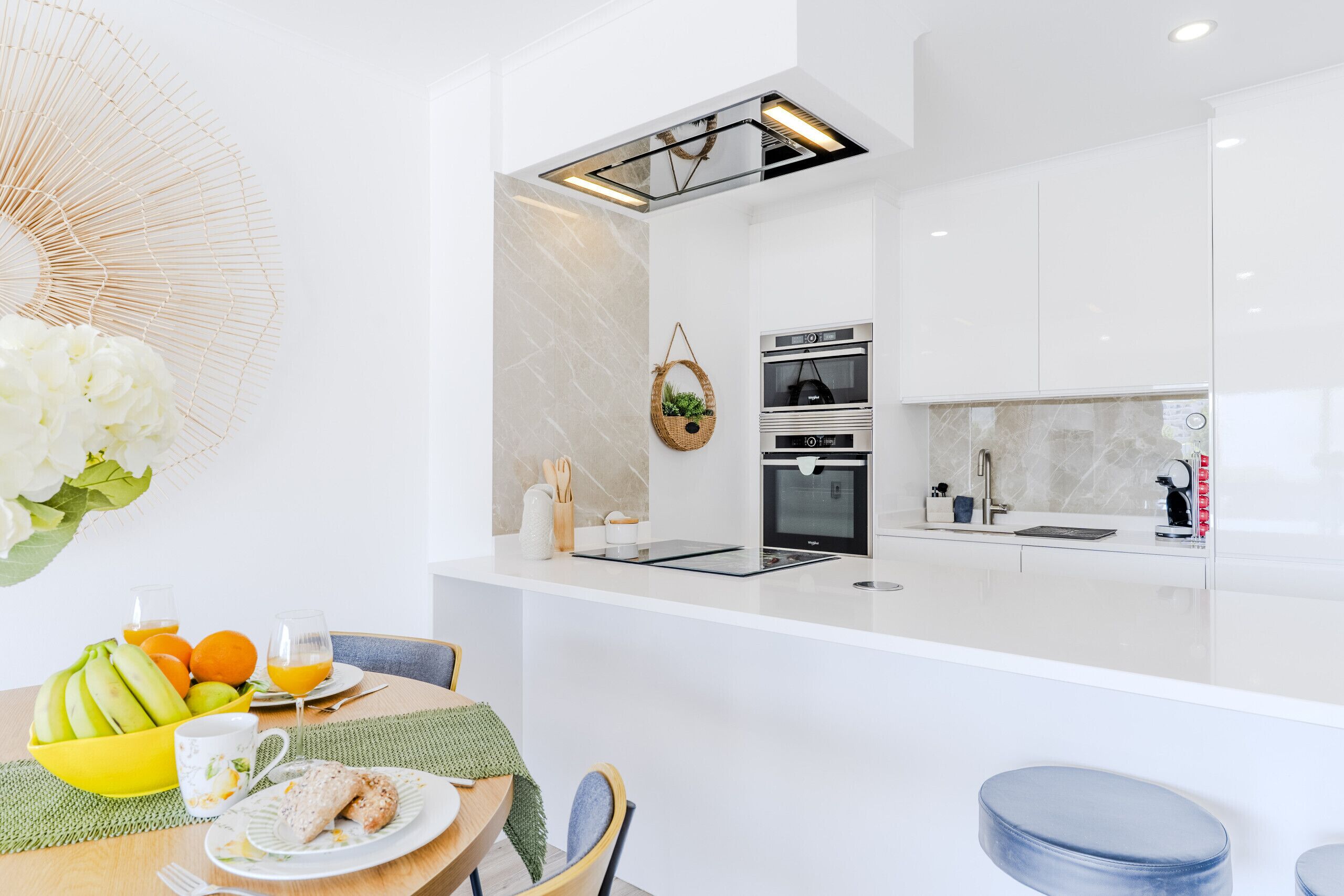 A modern kitchen with a built-in oven, a sink, and a dining area with a table set for breakfast.