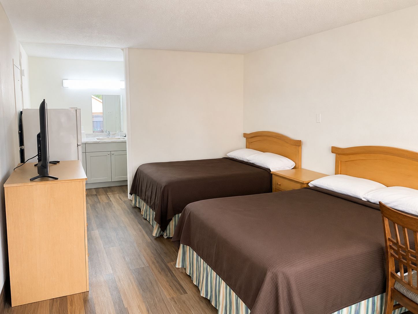 A hotel room with two beds, a desk, and a kitchenette.