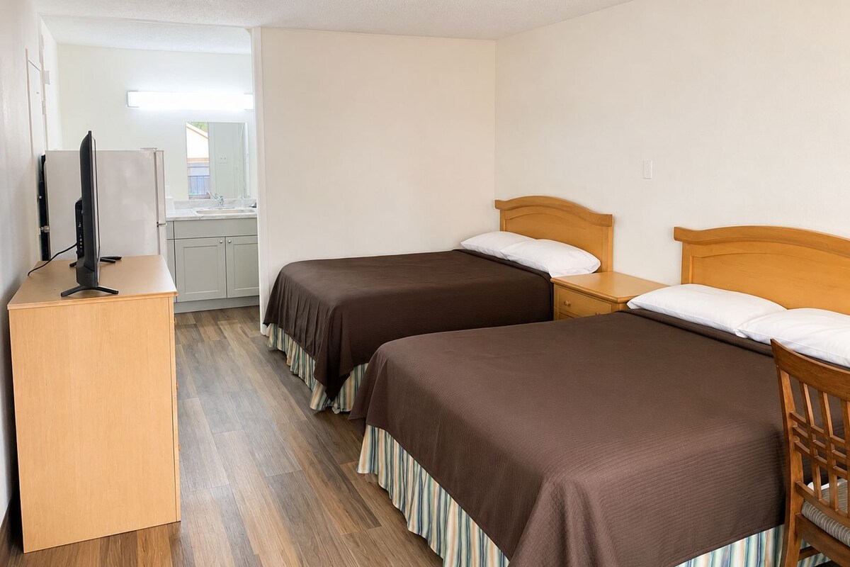 A hotel room with two beds, a desk, and a kitchenette.