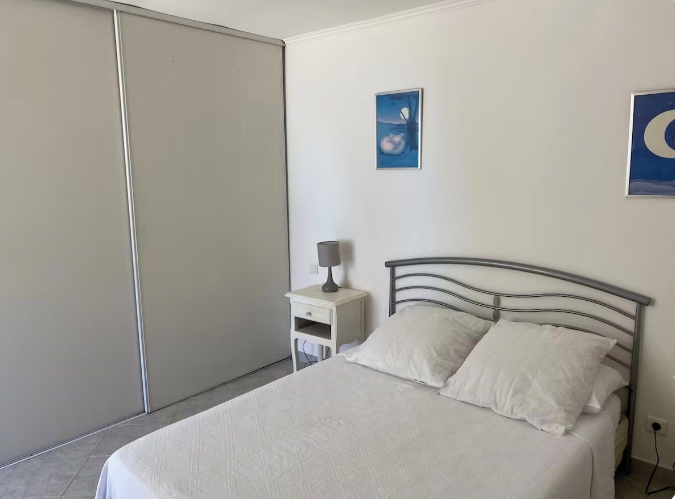 Une chambre à coucher avec un lit, une table de chevet, une lampe et un tableau accroché au mur.