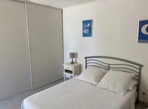 A bedroom with a bed, a nightstand, a lamp, and a wall-mounted picture. - Vacation Rental: Single-Family Home (Sartène)
