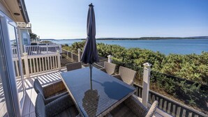 En balkon med et bord og stole, med udsigt over vandet.