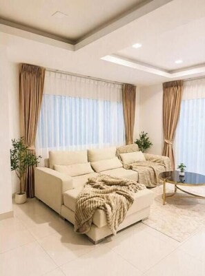 A modern living room with a beige sofa, a coffee table, and curtains. - Paradise Away From Home | Elegant Lakeview Villa with Pool in Central Pattaya (Chon Buri)