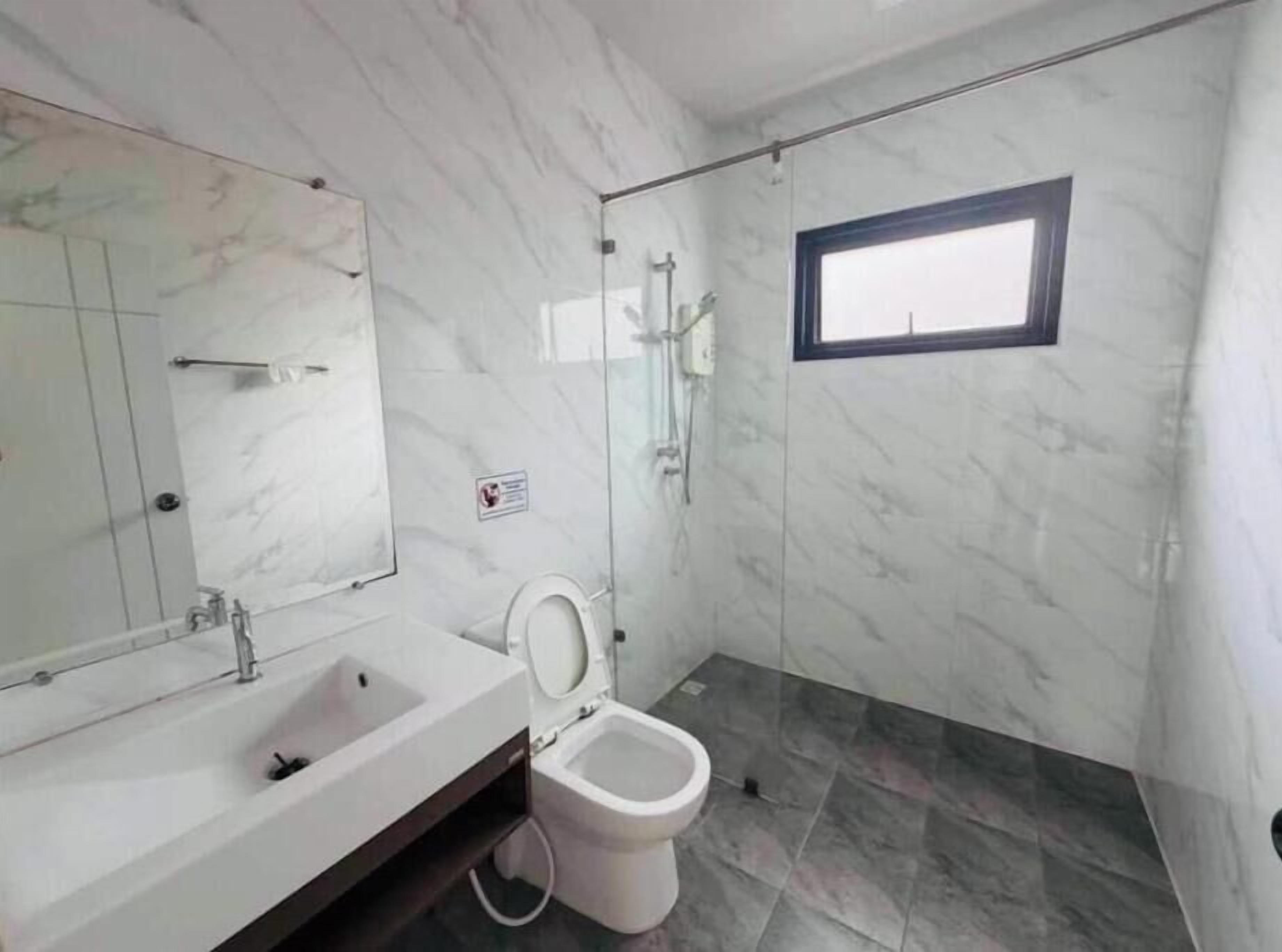 A bathroom with a marble wall, a sink, a toilet, and a shower area.
