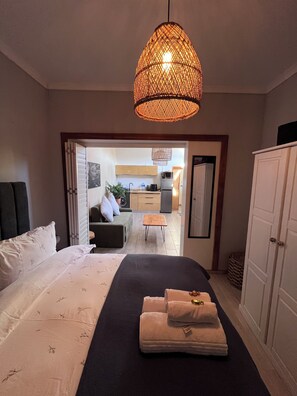 Une chambre d’hôtel avec un lit, une table de chevet avec des serviettes, un luminaire suspendu, une vue sur la cuisine et une armoire.