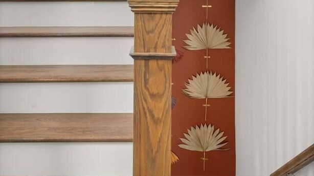 Eine Treppe mit Holzboden und Holzhandlauf, die zu einer Empore mit roter Wand und dekorativen Blattmustern führt.