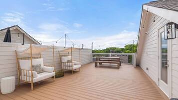 A wooden deck with outdoor seating, including two chairs and a bench, and a canopy structure.