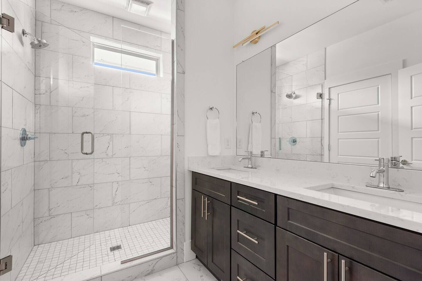 Un baño moderno con cabina de ducha, un espejo grande y muebles oscuros.