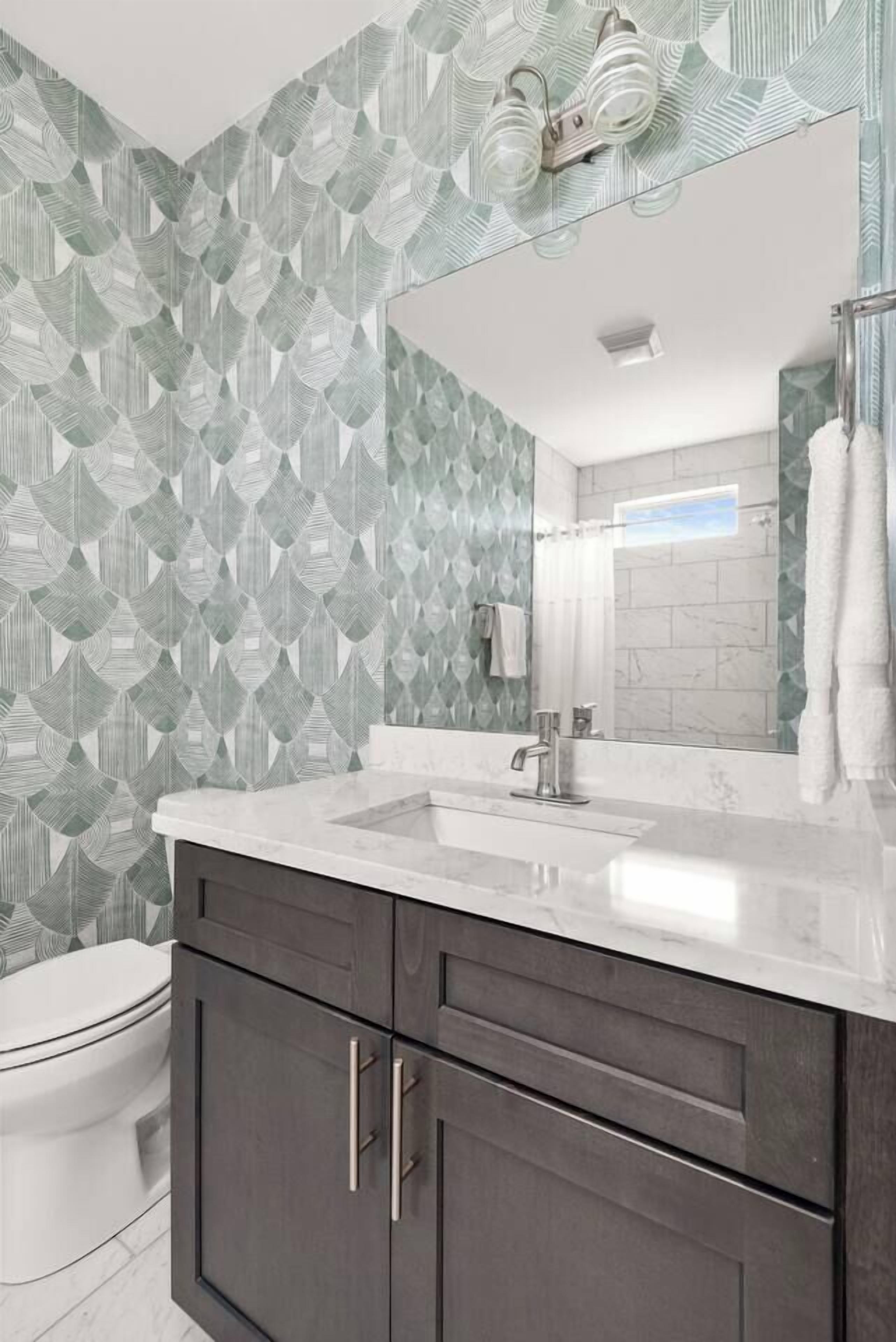 Une salle de bain avec un papier peint à motifs, un lavabo blanc, des meubles sombres et un miroir.