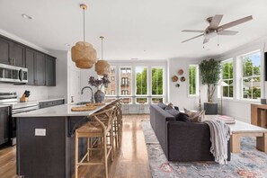 A modern kitchen with a central island, dark cabinetry, and a dining area with a sofa and chairs. - Soak it up in East! 8 beds 3.5 bath Garage incl! (Nashville)