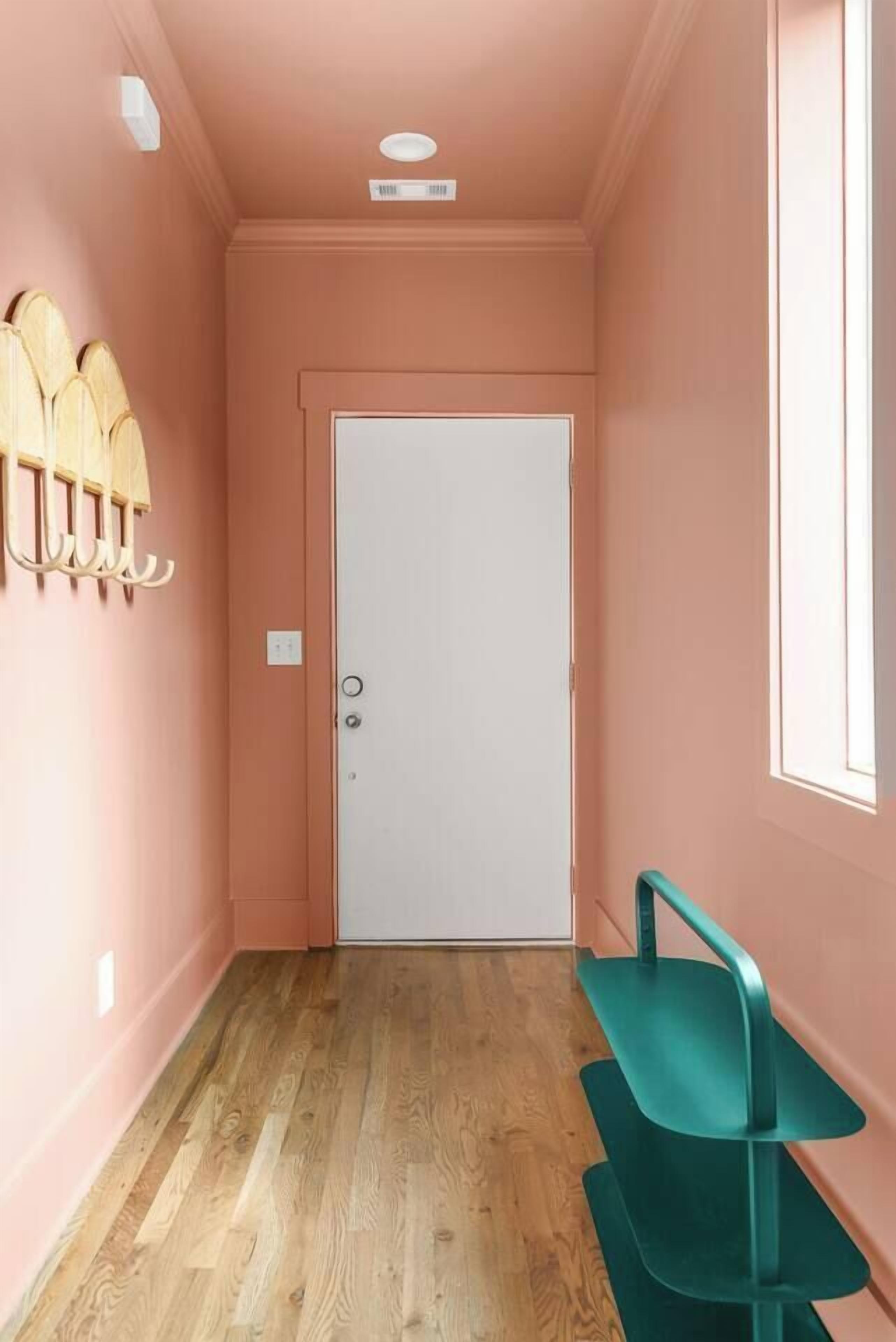 A hallway with a white door, wooden floor, and a green bench.