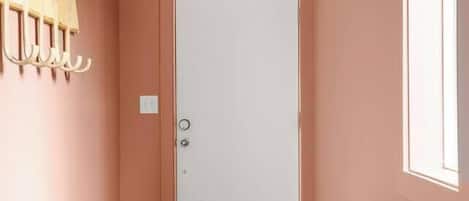 A hallway with a white door, wooden floor, and a green bench.