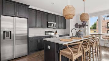 A modern kitchen with dark cabinets, stainless appliances, a central island with bar stools, and a large window offering a view.