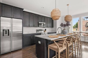 A modern kitchen with dark cabinets, stainless appliances, a central island with bar stools, and a large window offering a view. - Soak it up in East! 8 beds 3.5 bath Garage incl! (Nashville)