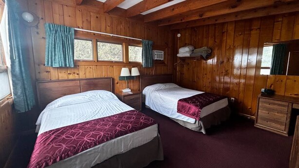 A wooden cabin room with two beds, a nightstand, a lamp, and a small dresser. - Cozy 1BR hotel room, Hamilton - #341 Rode-A-Syde (Hamilton)
