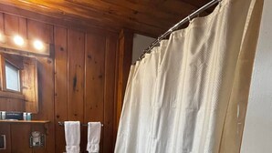 A bathroom with a wooden ceiling, a white toilet, a sink, and a shower curtain. - Cozy 1BR hotel room, Hamilton - #341 Rode-A-Syde (Hamilton)
