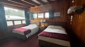 A cabin-style room with two beds, a window with curtains, a nightstand, and a wall-mounted heater. - Cozy 1BR hotel room, Hamilton - #341 Rode-A-Syde (Hamilton)
